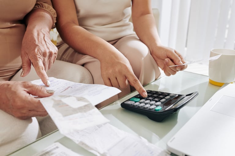 Two people reviewing financial documents and using a calculator together at a white desk