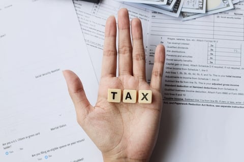 Open hand holding wooden letter blocks spelling TAX, with tax forms in the background