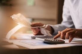Person using calculator and reviewing financial documents at desk with laptop
