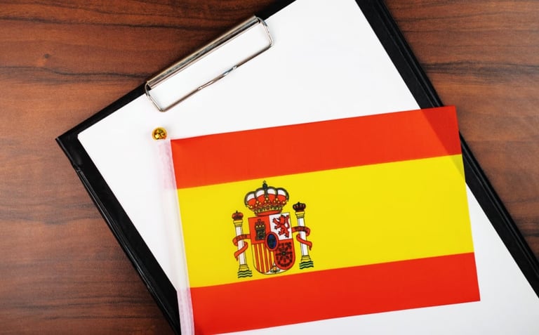 Spanish flag with coat of arms on clipboard with white paper on wooden desk