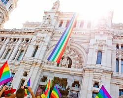 Pride parade attendees holding rainbow flags in front of an ornate white government building